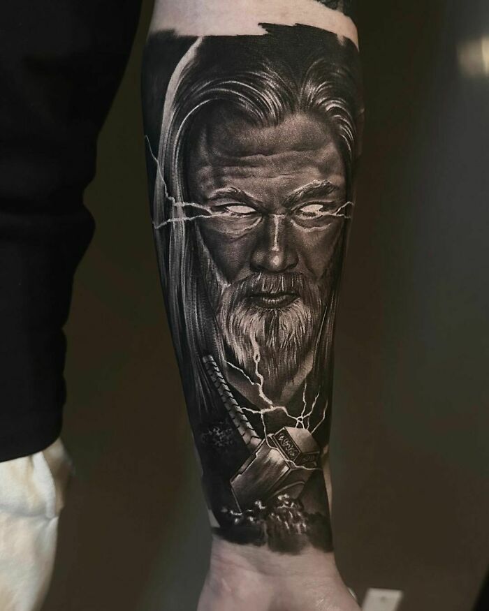 A forearm tattoo depicting a realistic Norse god with lightning details and a powerful hammer.