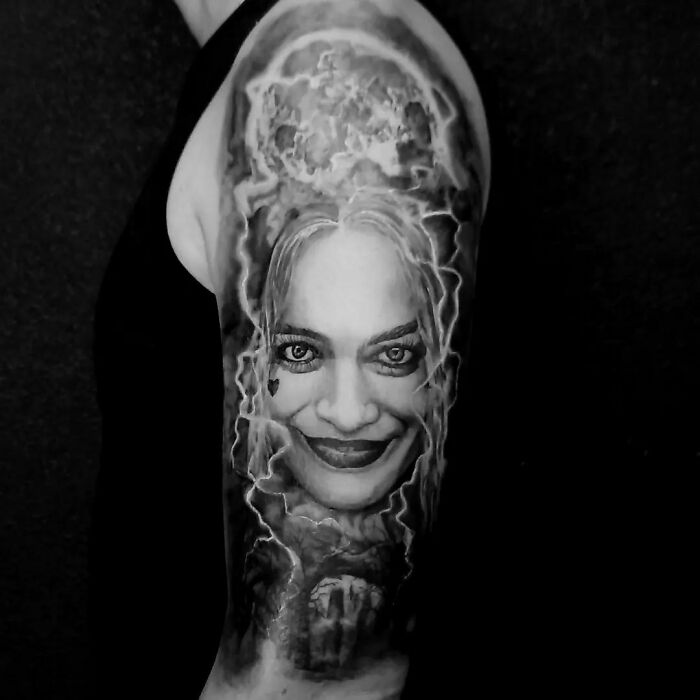 Super realistic tattoo of a smiling face with stormy background on upper arm.