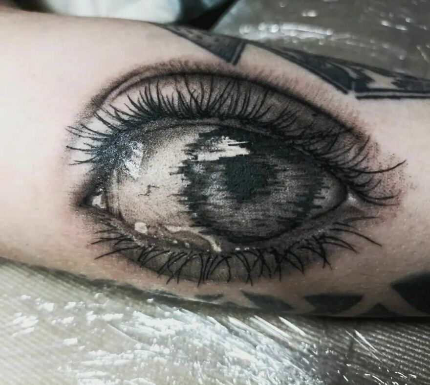 Realistic eye tattoo on arm, showcasing intricate detail and shading.