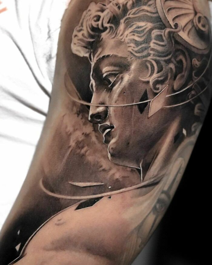 Realistic tattoo of a detailed classical sculpture on an arm, showcasing artistic tattoo design.