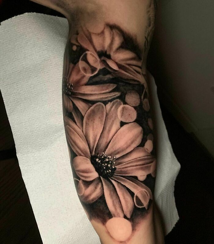 Realistic tattoo of flowers on an arm, showcasing detailed petal designs and shading.