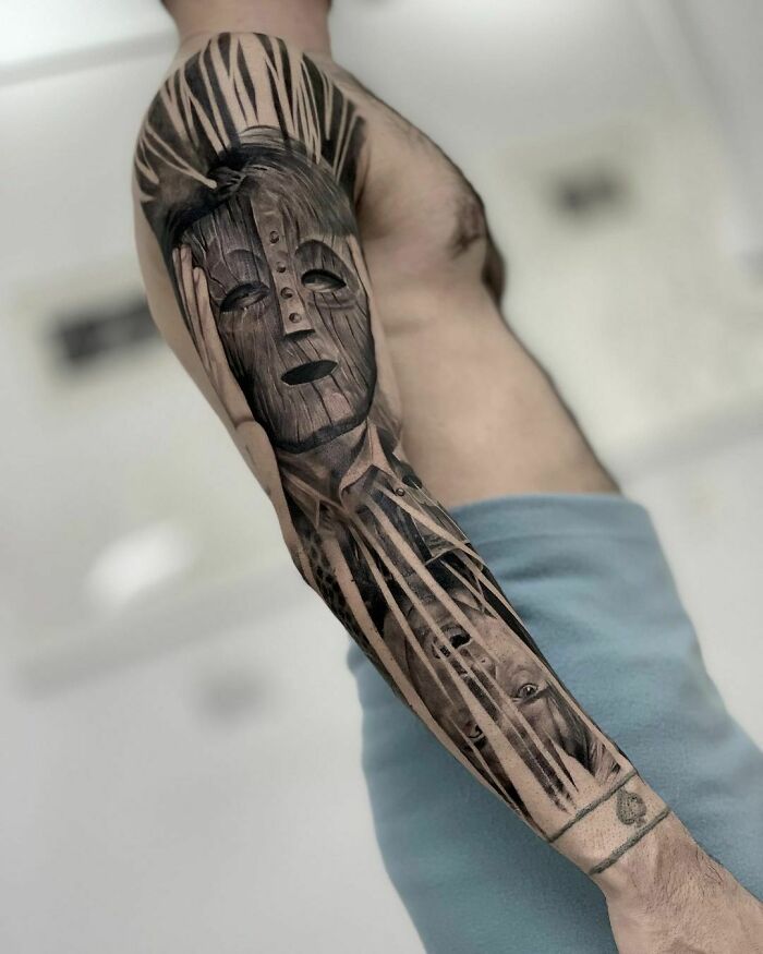 Super realistic tattoo sleeve featuring an intricate tribal mask design on a man's arm.