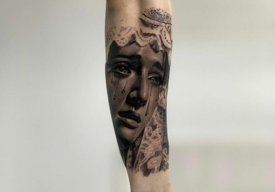Super realistic tattoo of a crying woman's face with intricate lace details on an arm.