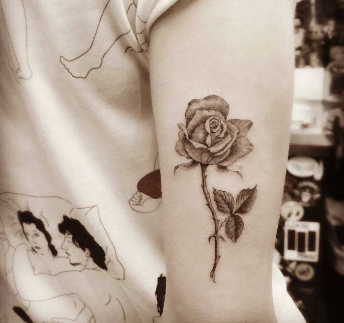 Celebrity tattoo of a detailed rose on an arm, with artistic shirt in background.