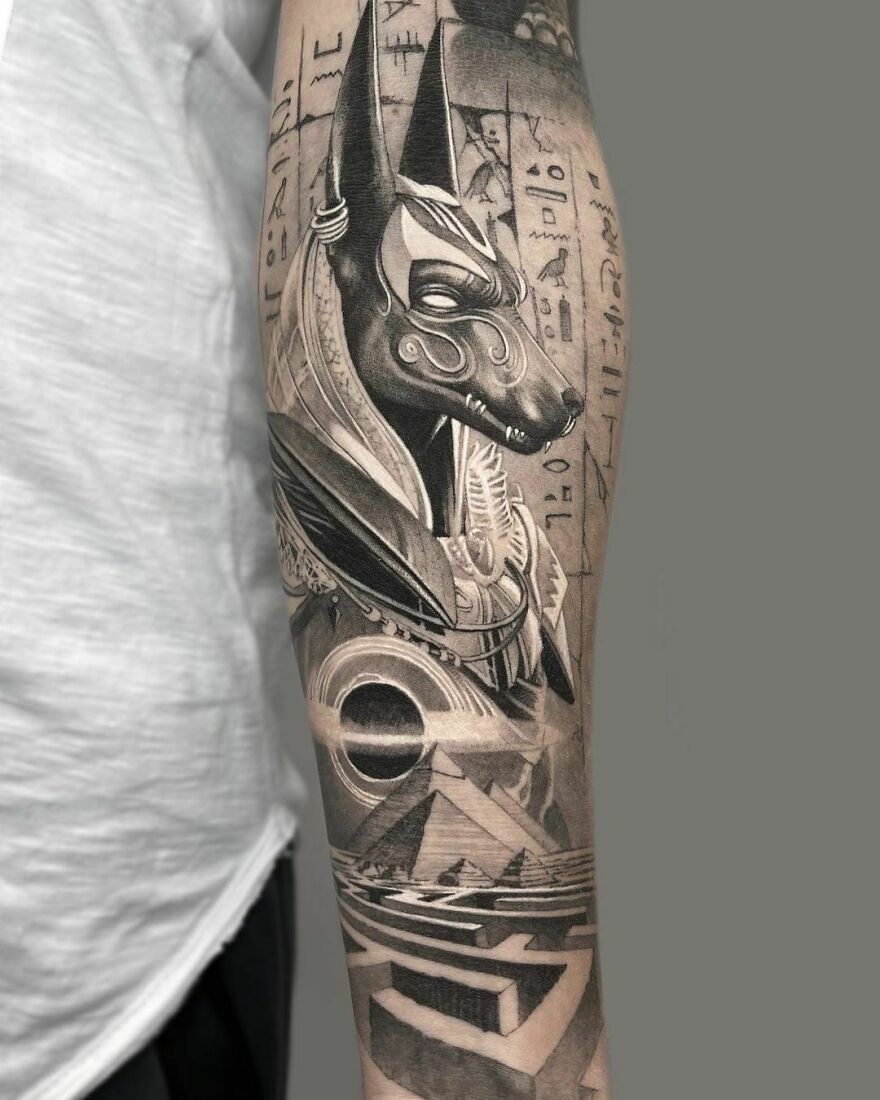 Realistic Anubis arm sleeve tattoo with intricate Egyptian details.