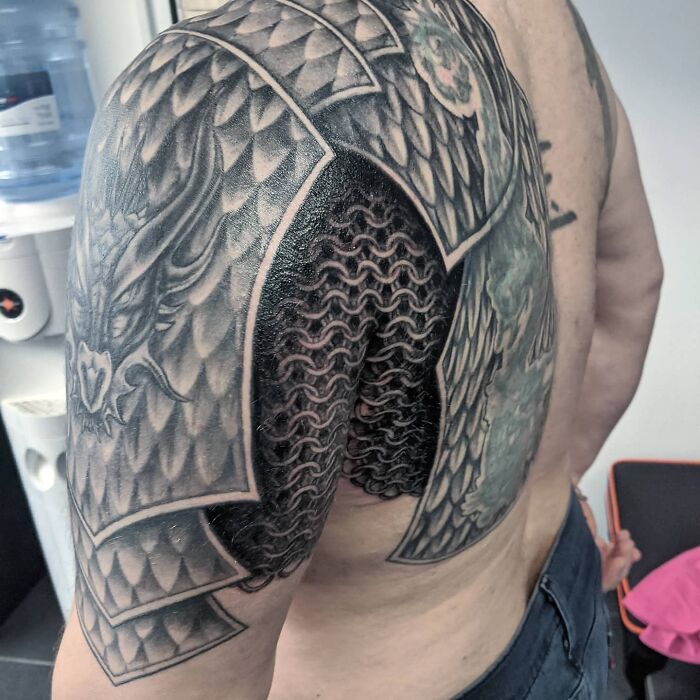 A super realistic tattoo of dragon scales and chainmail on a man’s shoulder and back.