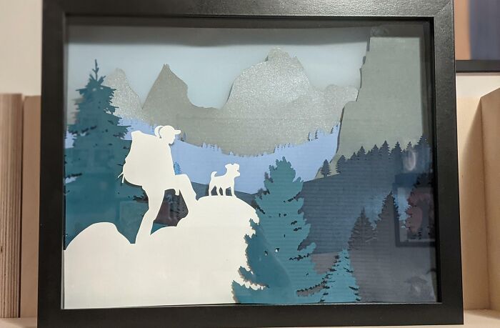 paper picture in a frame with human and a dog in the mountains