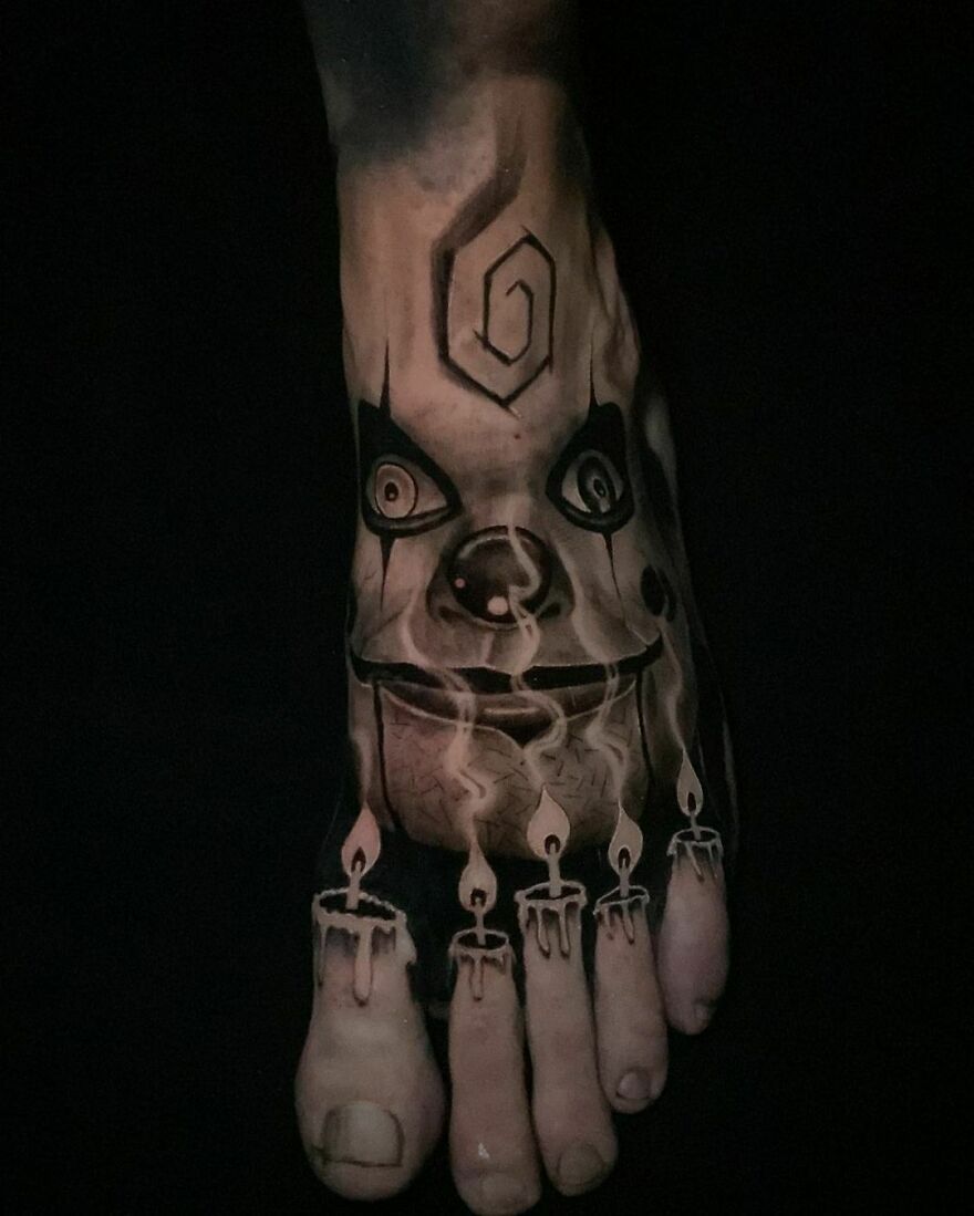 Foot tattoo with realistic detailing of Dead Silence doll face and fingers as candles.