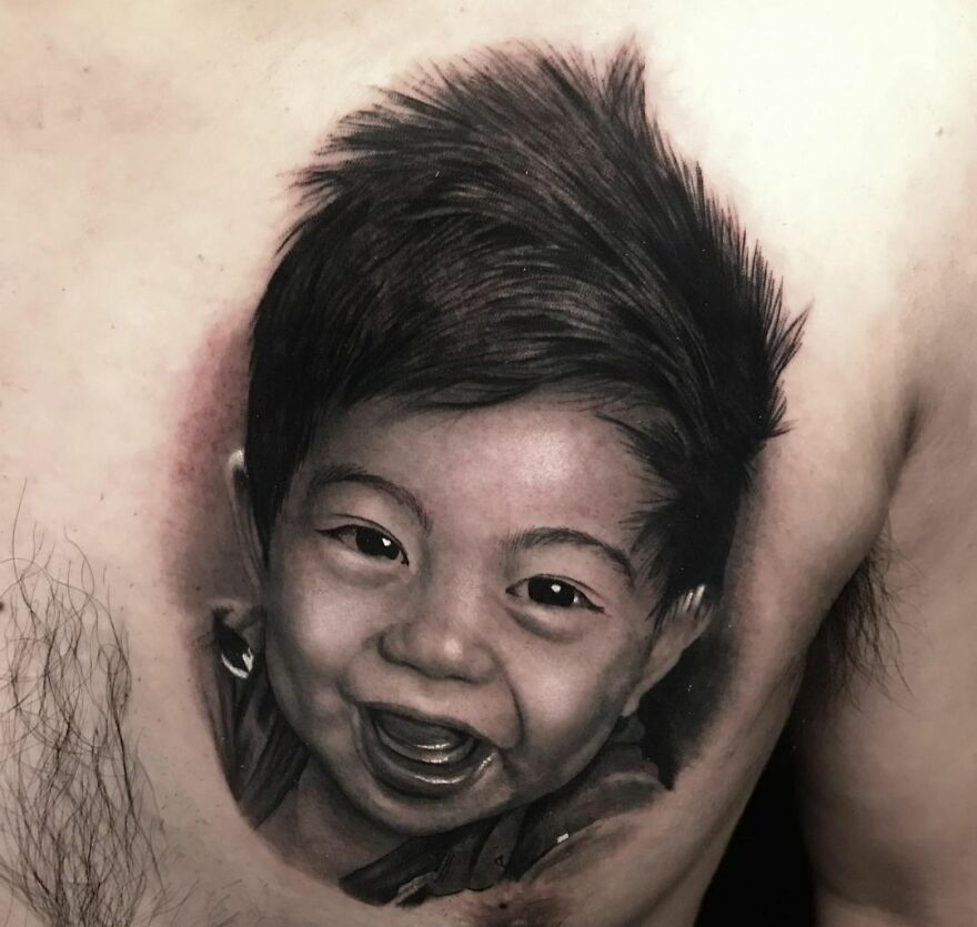 Super realistic tattoo of a happy Japanese baby with soft black hair on chest, showcasing intricate detailing.