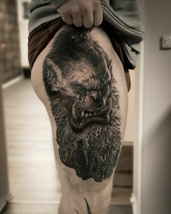 Realistic tattoo of an orc face on a person's thigh, showcasing intricate details and shading.