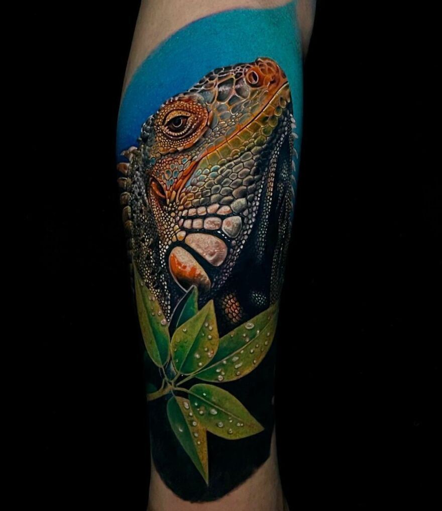 Super realistic tattoo of an iguana with vivid colors and detailed textures on the skin, featuring green leaves.