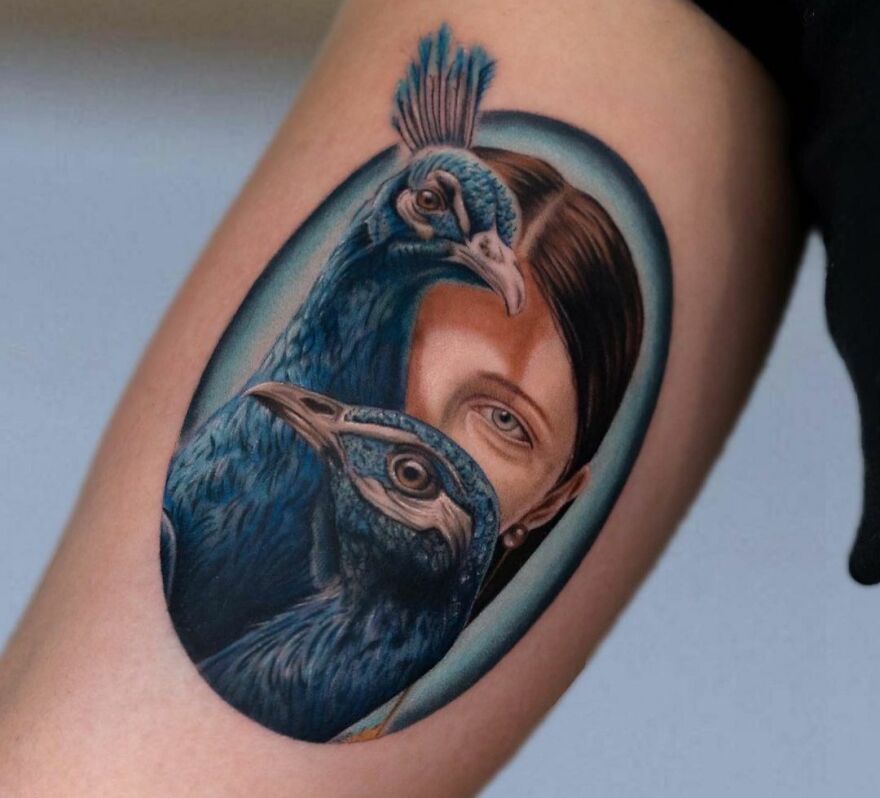 Realistic tattoo of a peacock and woman's face, showcasing intricate and vibrant detail.