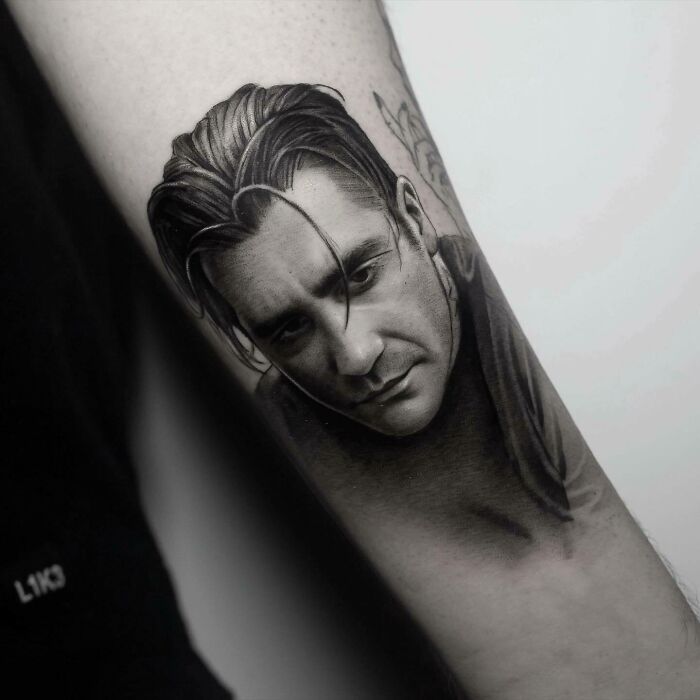 Realistic tattoo of a man's face on a forearm, showcasing detailed shading and lifelike expression.