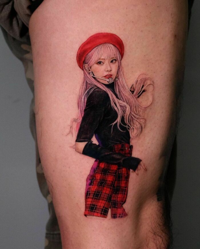 Realistic tattoo of a woman with long pink hair, wearing a red beret and plaid skirt on a person's thigh.