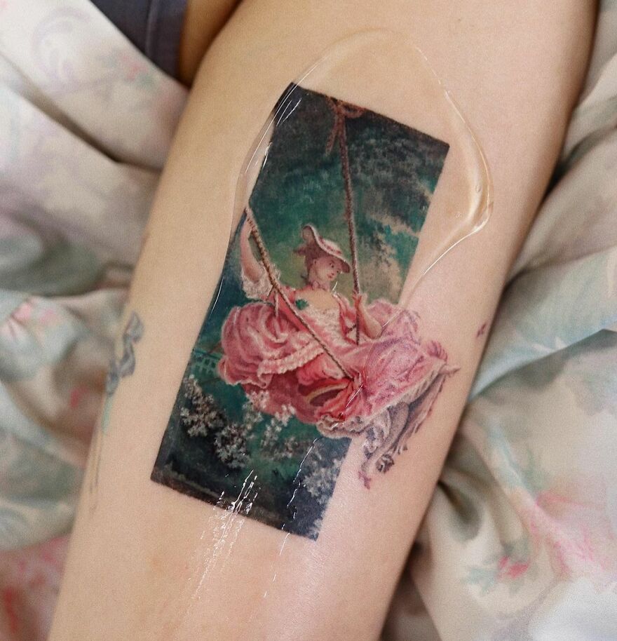 Realistic tattoo of a woman in a pink dress on a swing, inspired by classical art, on a person's arm.