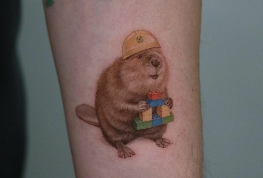 Super realistic tattoo of a beaver wearing a hard hat and holding colorful blocks, showcasing amazing detail.