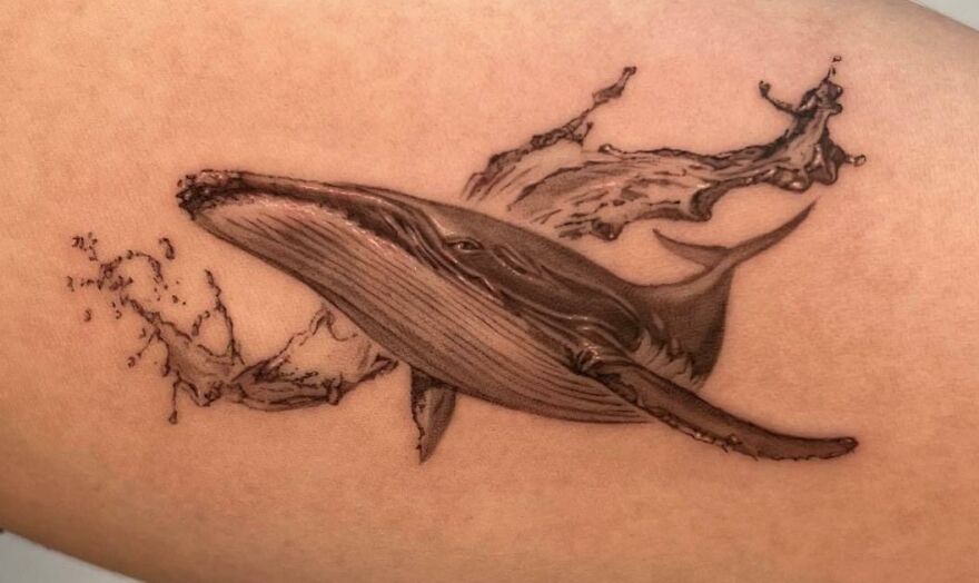 Realistic whale and splash tattoo with intricate detailing.