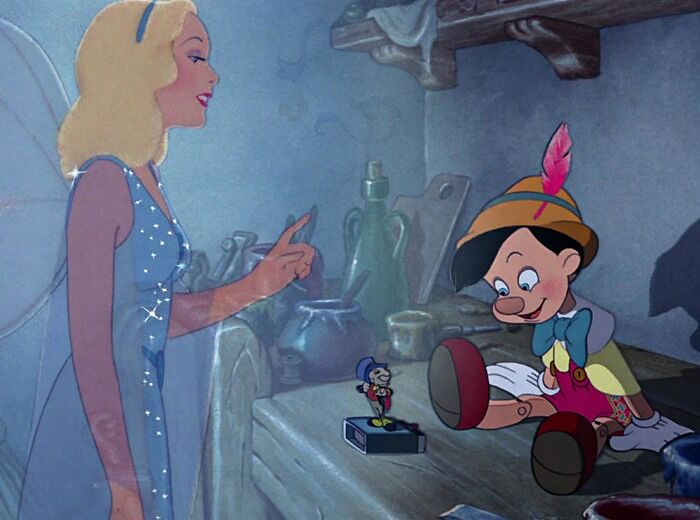 Fairy talking to Pinocchio in a workshop, with Jiminy Cricket nearby, depicting a relatable cartoon moment.