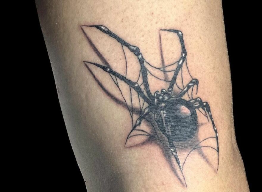 Realistic tattoo of a spider with detailed shading and web design on skin.