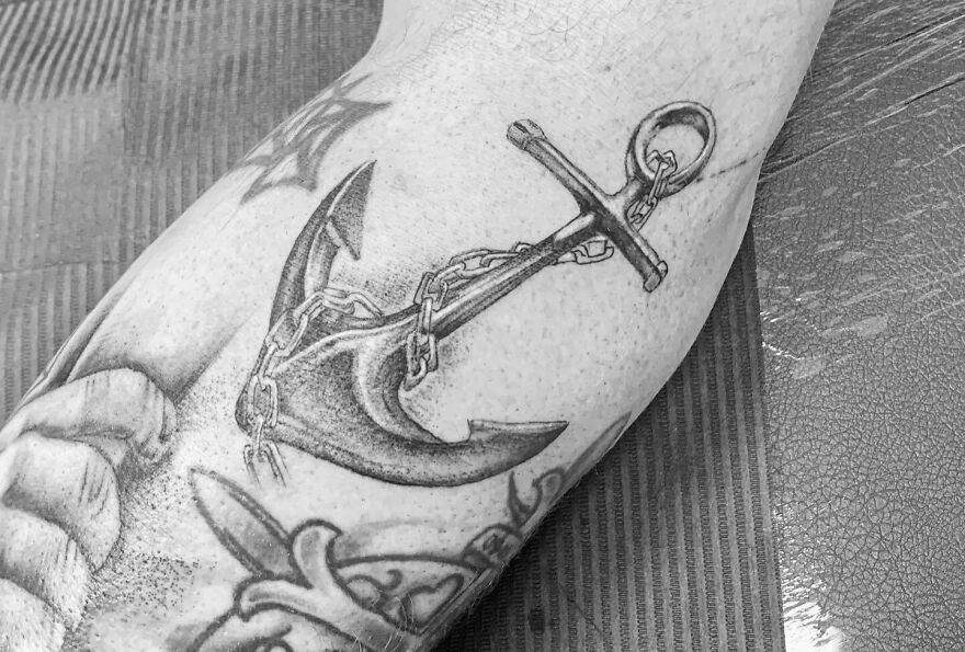 Black and gray realistic tattoo of an anchor with a chain on an arm, showcasing intricate detail and shading.