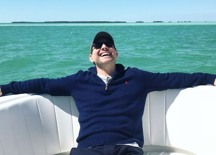 A man in a blue sweater and sunglasses relaxing on a boat.