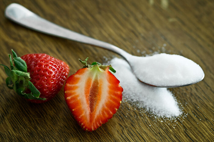 A spoonful of sugar and two strawberries on a wooden table