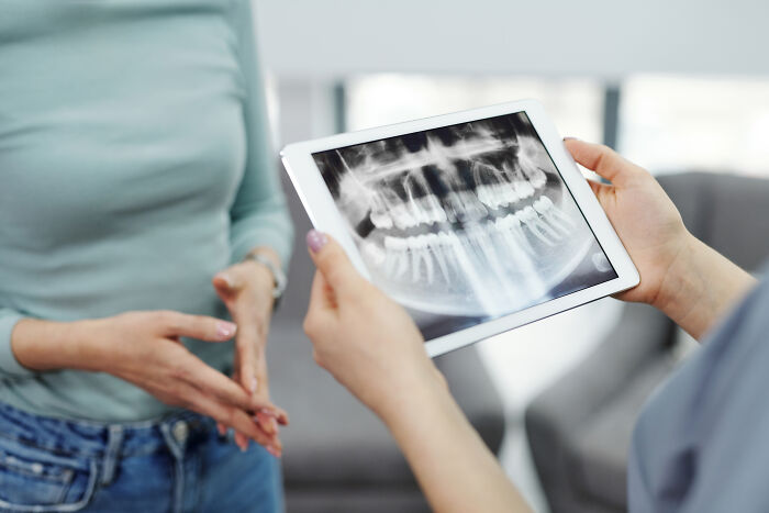 A person's hands holding an x-ray image of teeth and another woman standing in front