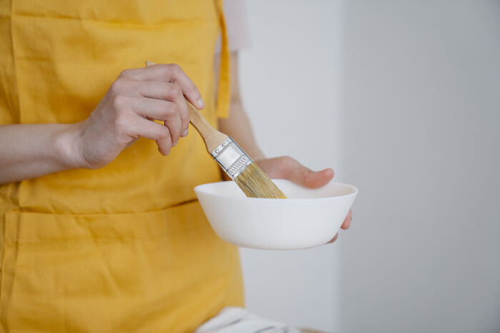 A person in a yellow apron holding a brush with a white bowl