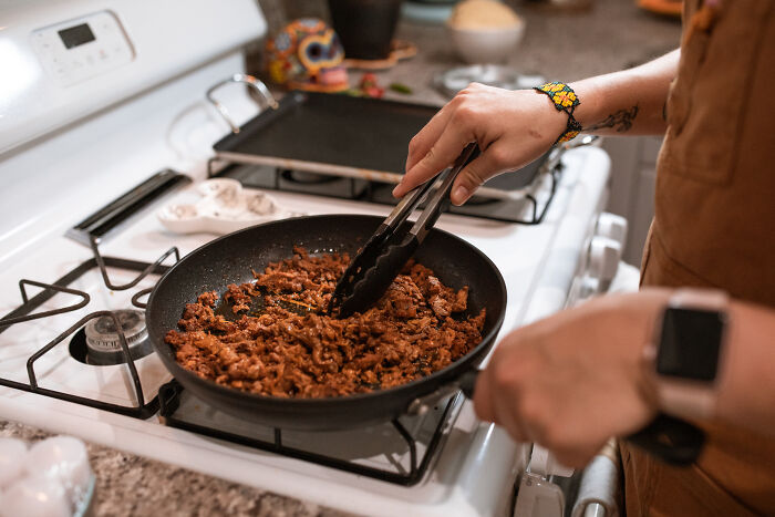 A person cooking meat in a black pan