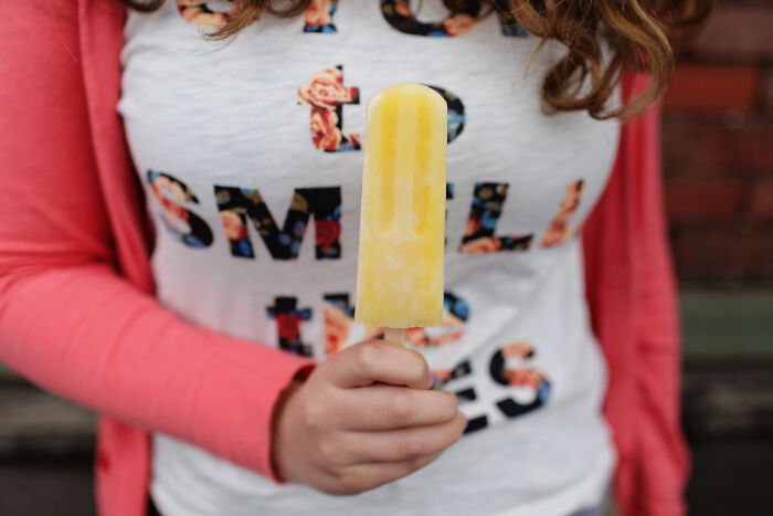 A woman in a pink sweater is holding a yellow popsicle