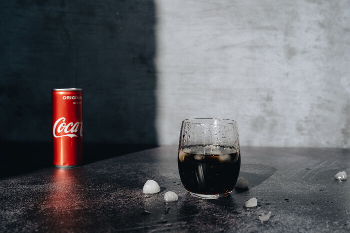 A glass of Coca-Cola with ice and a red can on the table