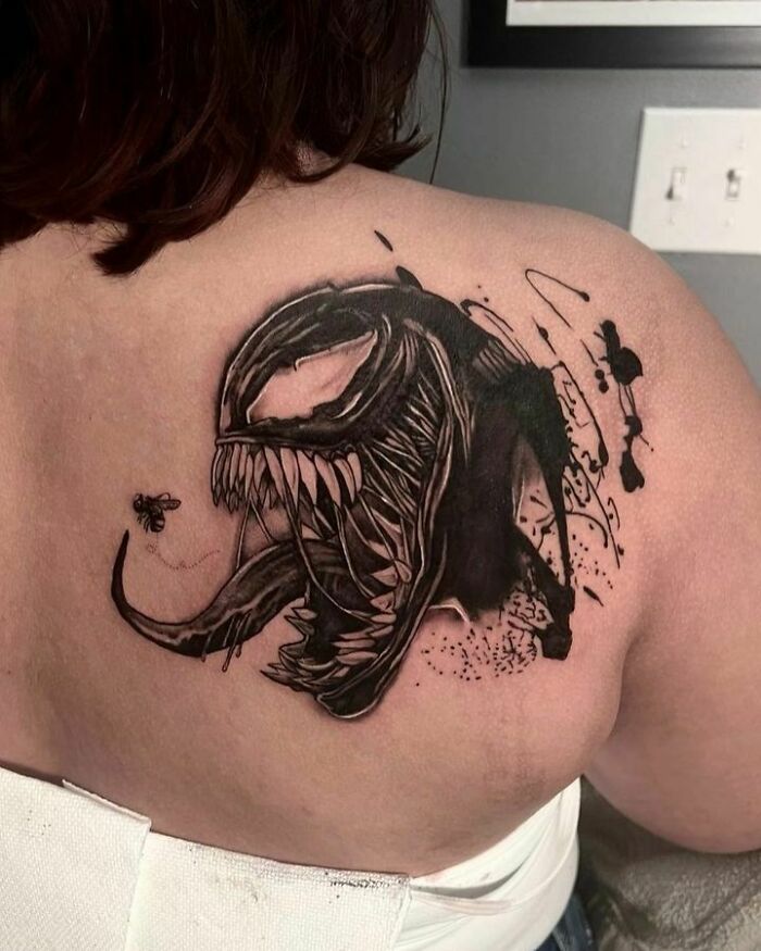 Marvel tattoo featuring Venom character on a person's upper back, showcasing intricate black ink design.