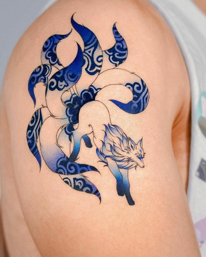 Blue and black artistic wolf tattoo with swirling patterns, symbolizing self-love, on upper arm.