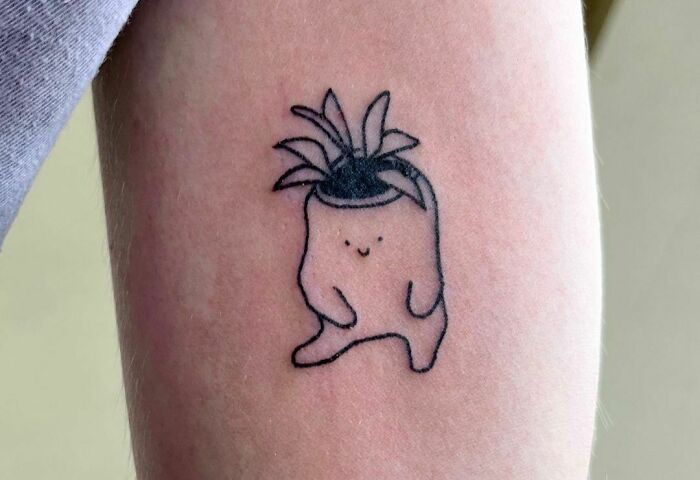 Cute self-love tattoo of a smiling plant creature on an arm.