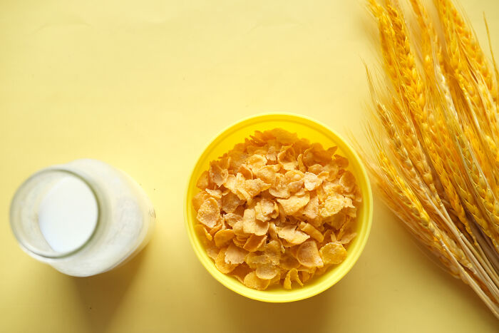 A yellow bowl with cornflakes, a carafe of milk, and wheat on the table