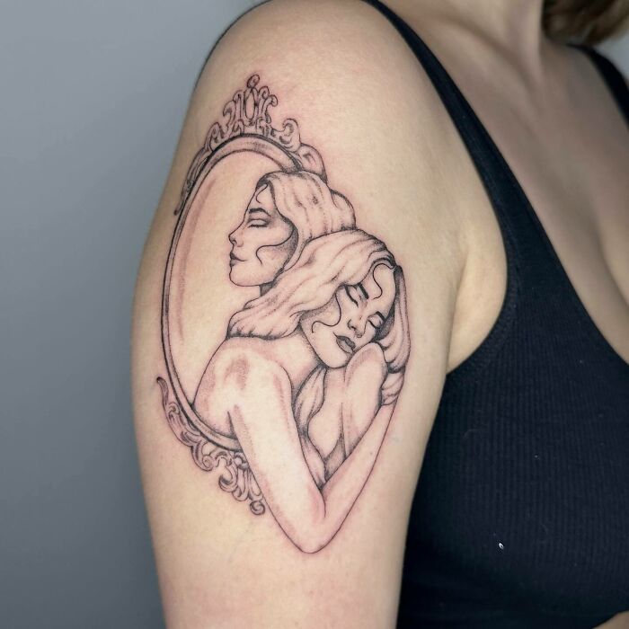 A self-love tattoo on a woman's arm features two figures embracing within an ornate mirror design.