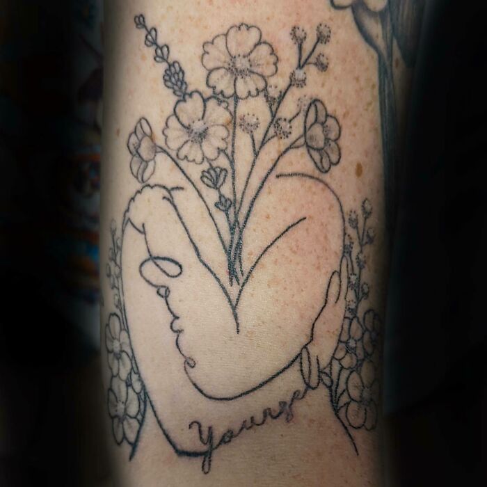 "Love yourself" person hugging herself with flowers tattoo 