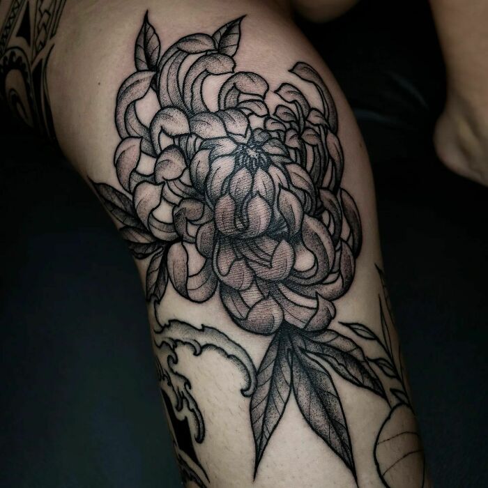 Elegant black ink flower tattoo on leg, showcasing intricate petal and leaf design.