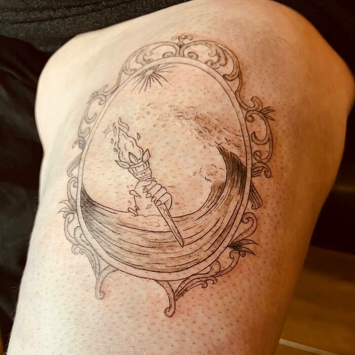 Self-love tattoo depicting a hand holding a torch within a decorative frame on skin.