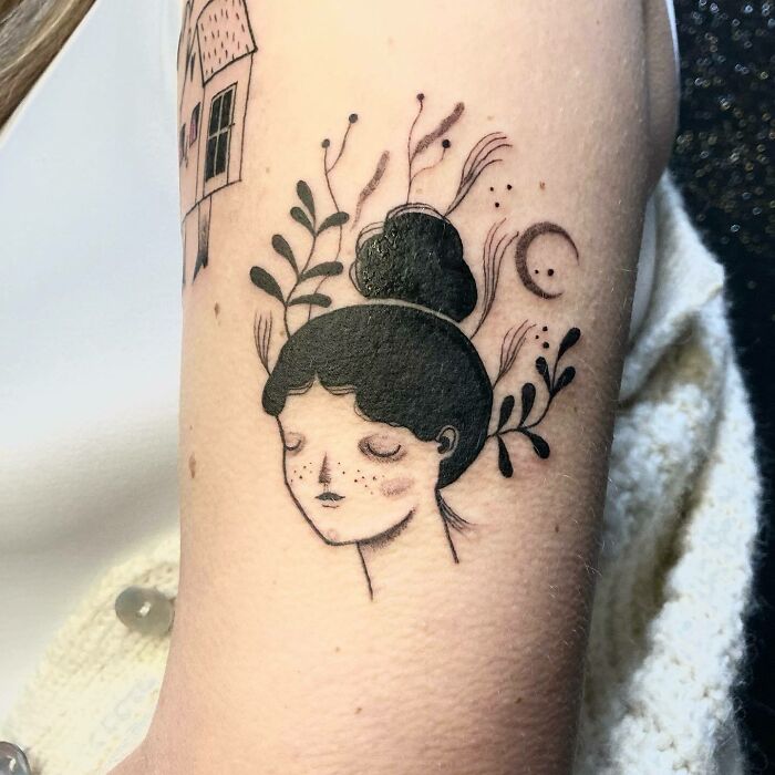 Tattoo of a serene woman with plant motifs, symbolizing self-love and empowerment, inked on an arm.