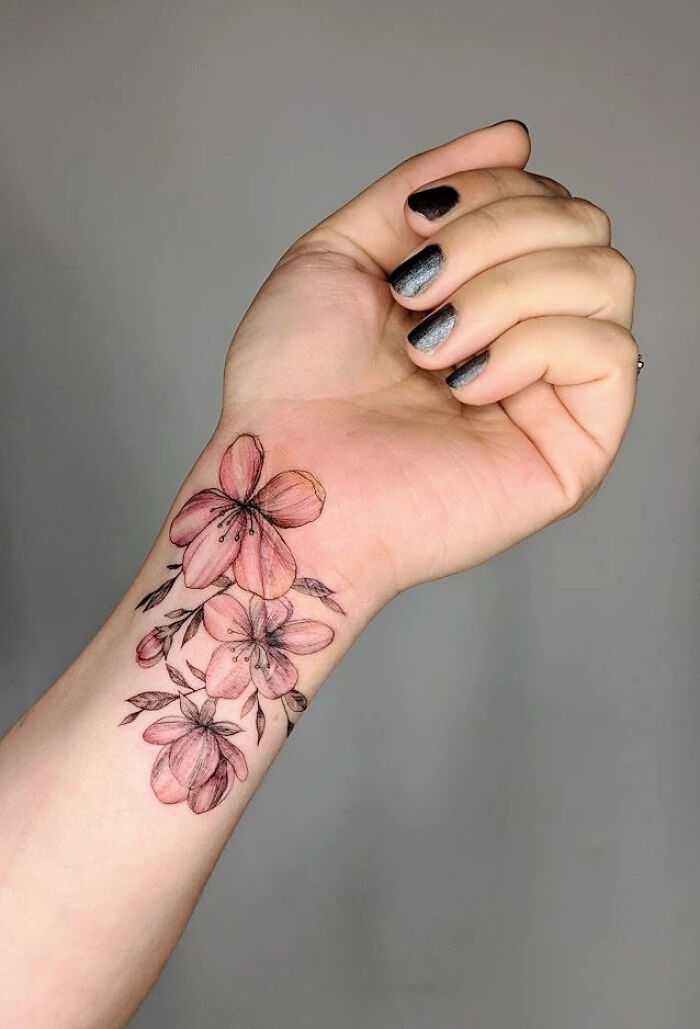 Elegant flower tattoo on forearm, showcasing delicate beauty with pink blossoms.