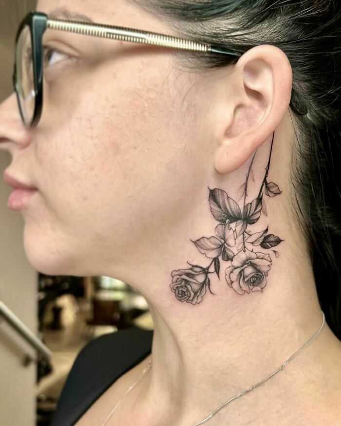 Elegant flower tattoo on neck, featuring detailed roses and leaves, showcasing beauty and artistic craftsmanship.