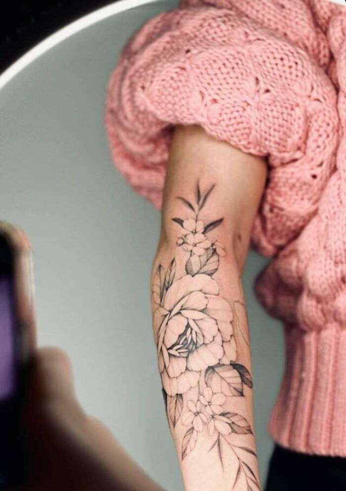 Elegant flower tattoo design on forearm, radiating beauty and style, worn with a pink knitted sweater.