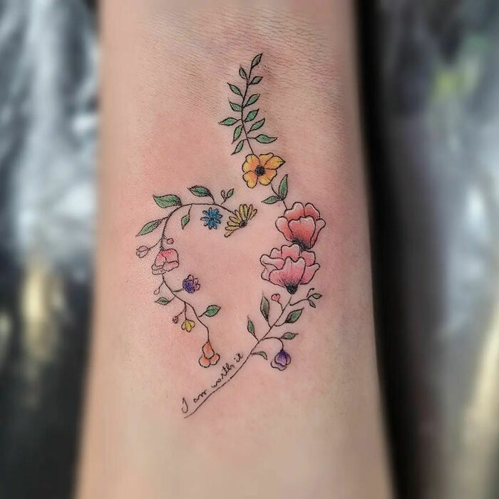 Delicate flower tattoo in a heart shape, featuring vibrant colors and leafy branches, radiates elegance and beauty.