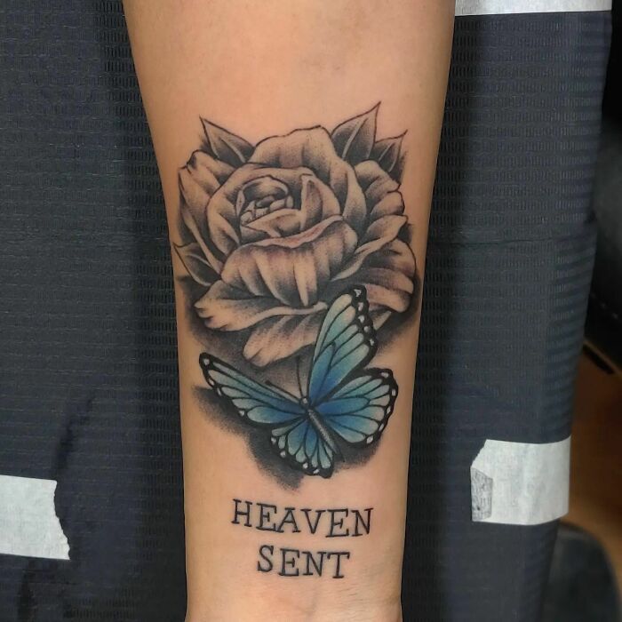 Flower tattoo with a blue butterfly on the forearm, featuring "Heaven Sent" text below the design.