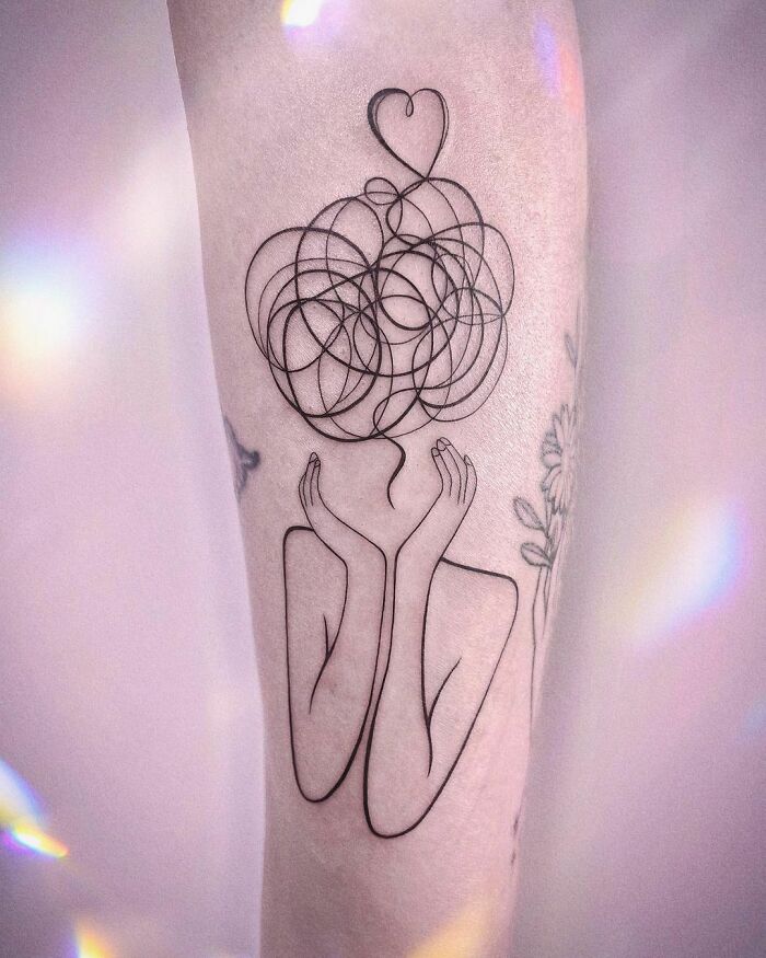 Line art self-love tattoo with a heart above abstract head design on inner forearm.