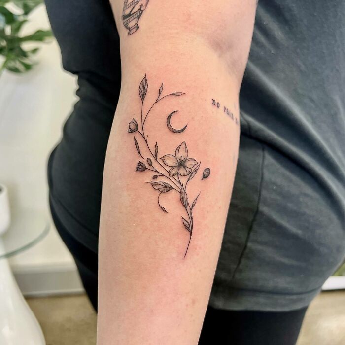Elegant flower tattoo on forearm with delicate line art and crescent moon design.