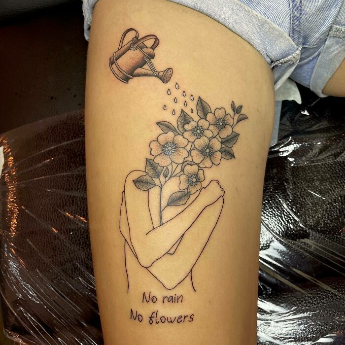 Self-love tattoo on a person's thigh, featuring flowers and a watering can, with the text "No rain, no flowers."