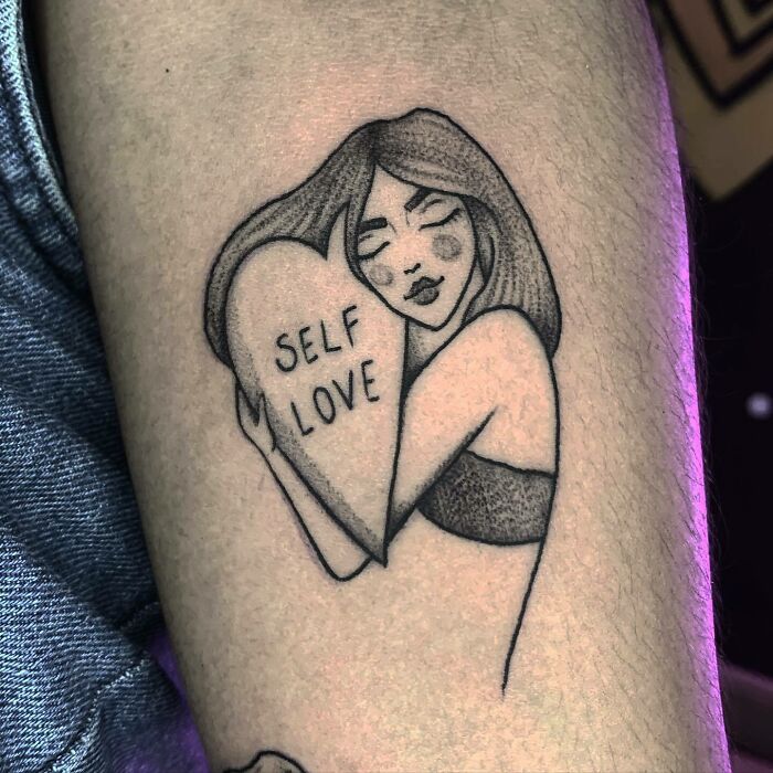 Woman hugging heart with "Self love" inscription tattoo 