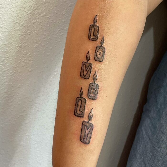 Self-love tattoo on arm with the word "LOVE" in candle-shaped letters.